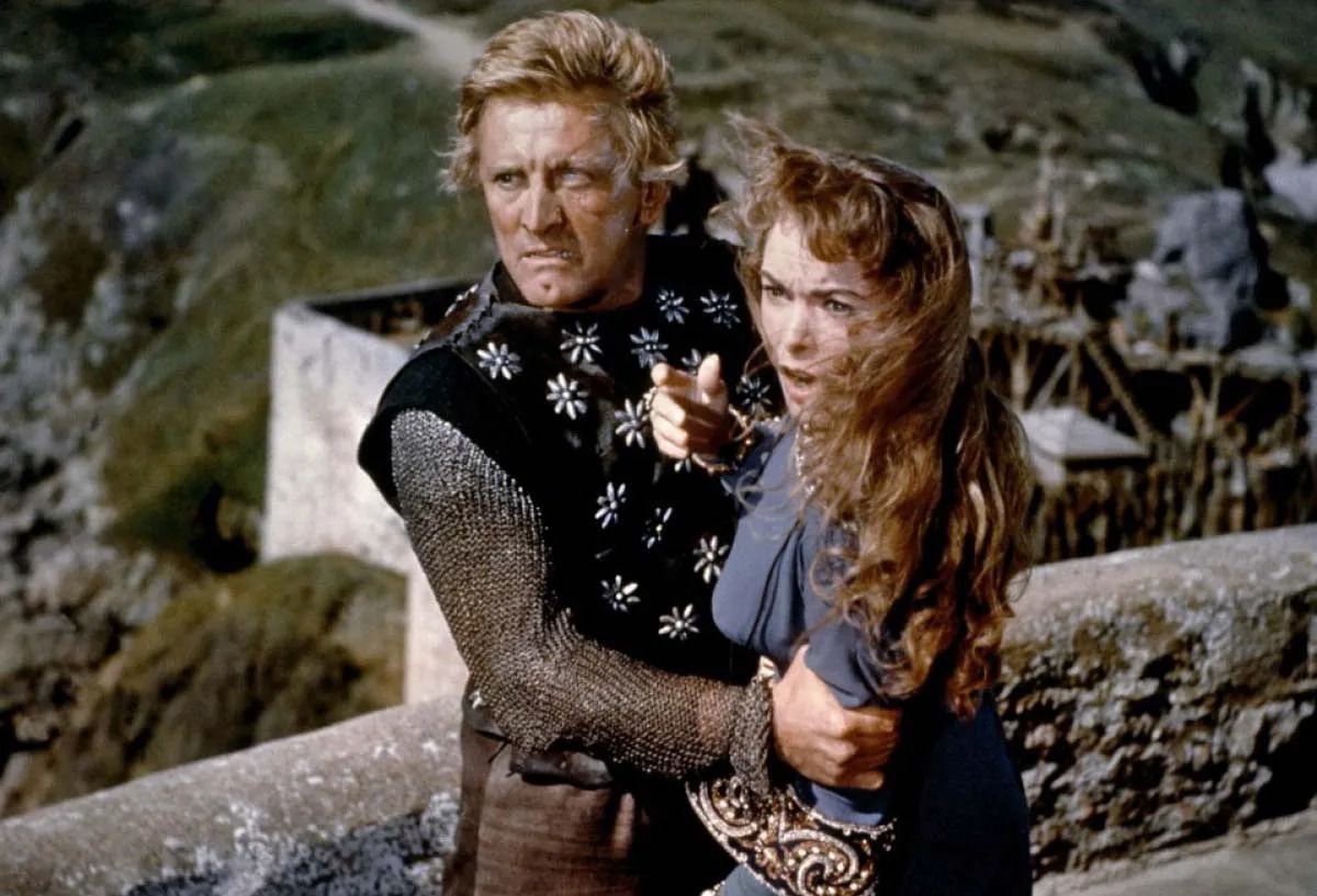 Un uomo in abiti vichinghi con un occhio cieco (Kirk Douglas) stringe gli occhi di una donna urlante che si affaccia su un balcone di pietra.