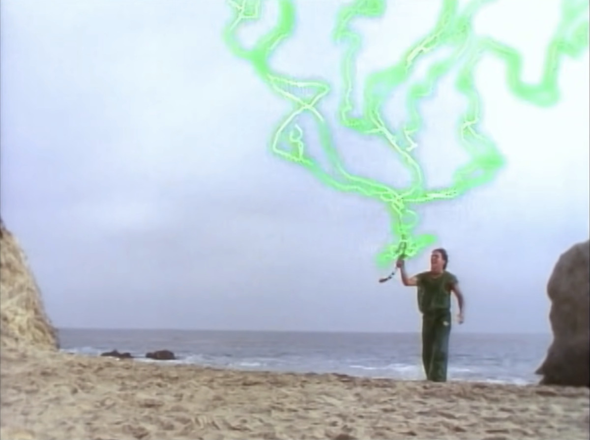 Tommy (Jason David Frank) in piedi su una spiaggia con una spada, tenendola sollevata mentre conduce un fulmine verde