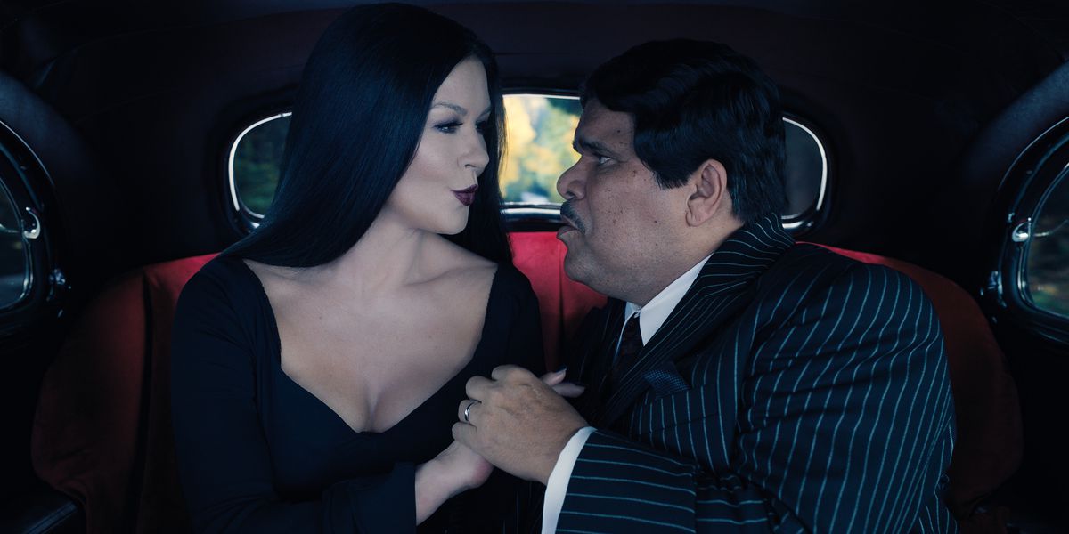 Morticia e Gomez si sbaciucchiano nel retro di un'auto.  entrambi sono vestiti di nero e si guardano adoranti negli occhi