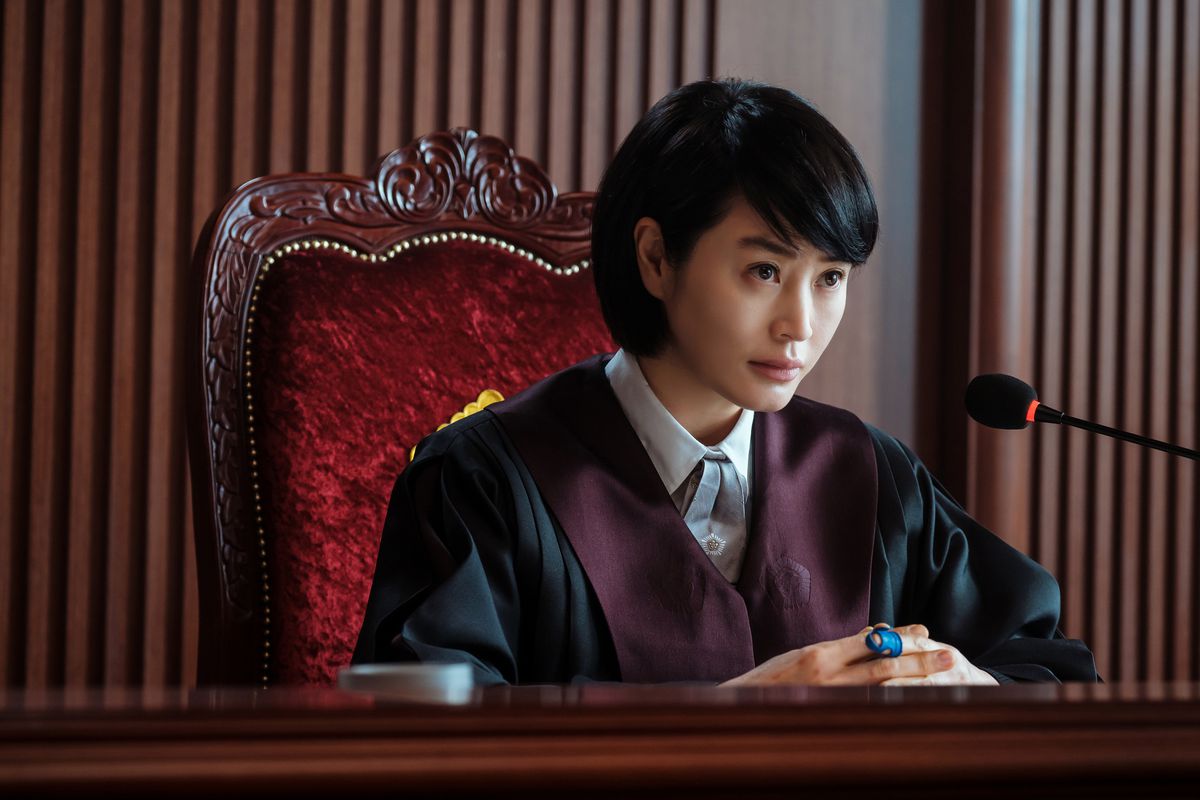 Kim Hye-soo indossa la toga del giudice e siede su una grande sedia rossa in Juvenile Justice.