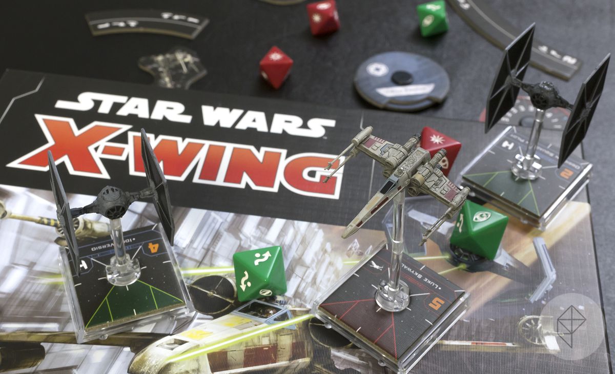 Tabellone e miniature di Star Wars: X-Wing Seconda Edizione, tra cui un X-Wing e due TIE Fighter insieme a dadi personalizzati, segnalini e altro ancora.