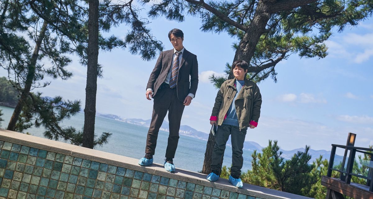 Il detective Hae-jun (Park Hae-il) è in piedi sul bordo di una piscina vuota con la testa piegata, guardando in basso con un'espressione perplessa, accanto a una collega che ha anche la testa piegata e uno sguardo perplesso simile , in un'immagine di Decision To Leave
