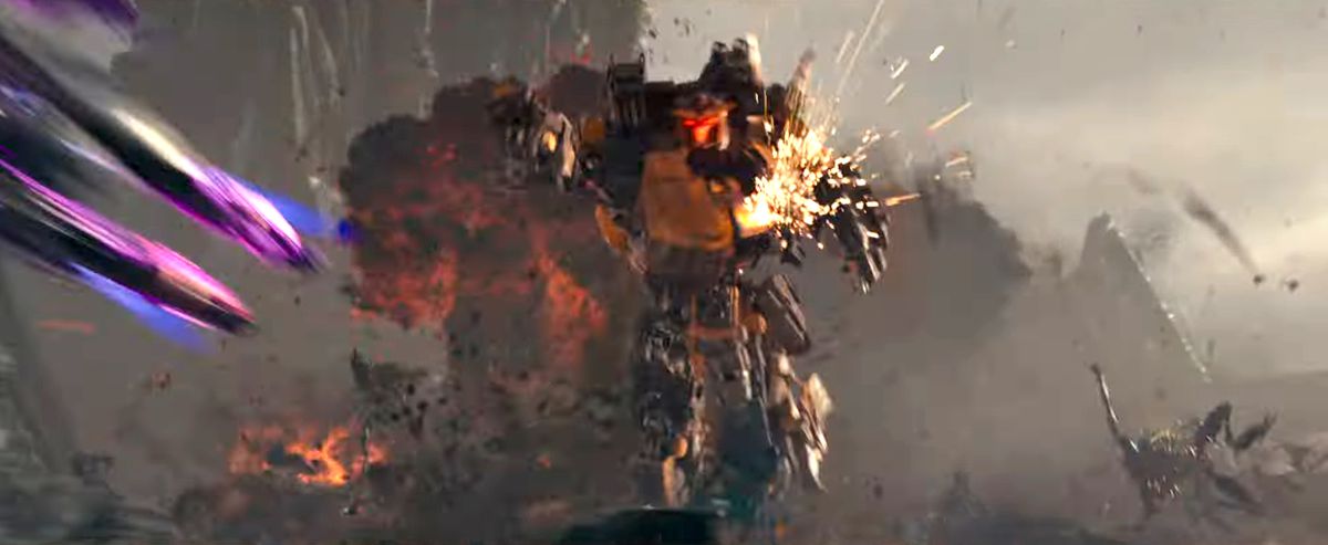 Un Transformer con gambe al neon viola sfreccia fuori dallo schermo mentre è inseguito da un trasformatore giallo con un'esplosione sullo sfondo in Transformers: Rise of the Beasts