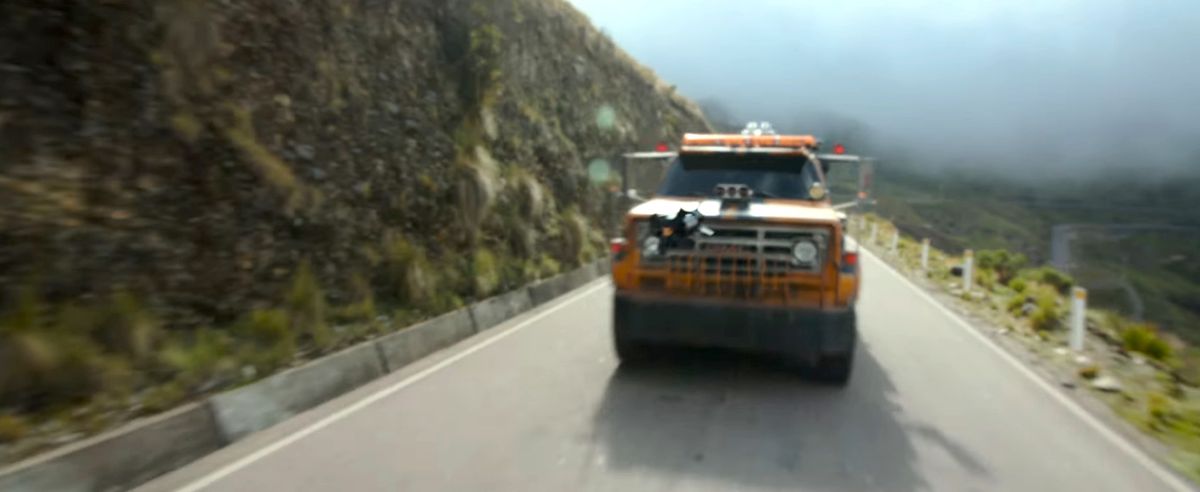 Un trasformatore giallo nascosto come un camion su un'autostrada in collina spara un missile Transformers: Rise of the Beasts