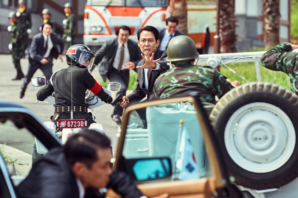 Lee Jung-jae tende la mano in una strada trafficata circondata da persone che corrono in giacca e cravatta a Hunt.