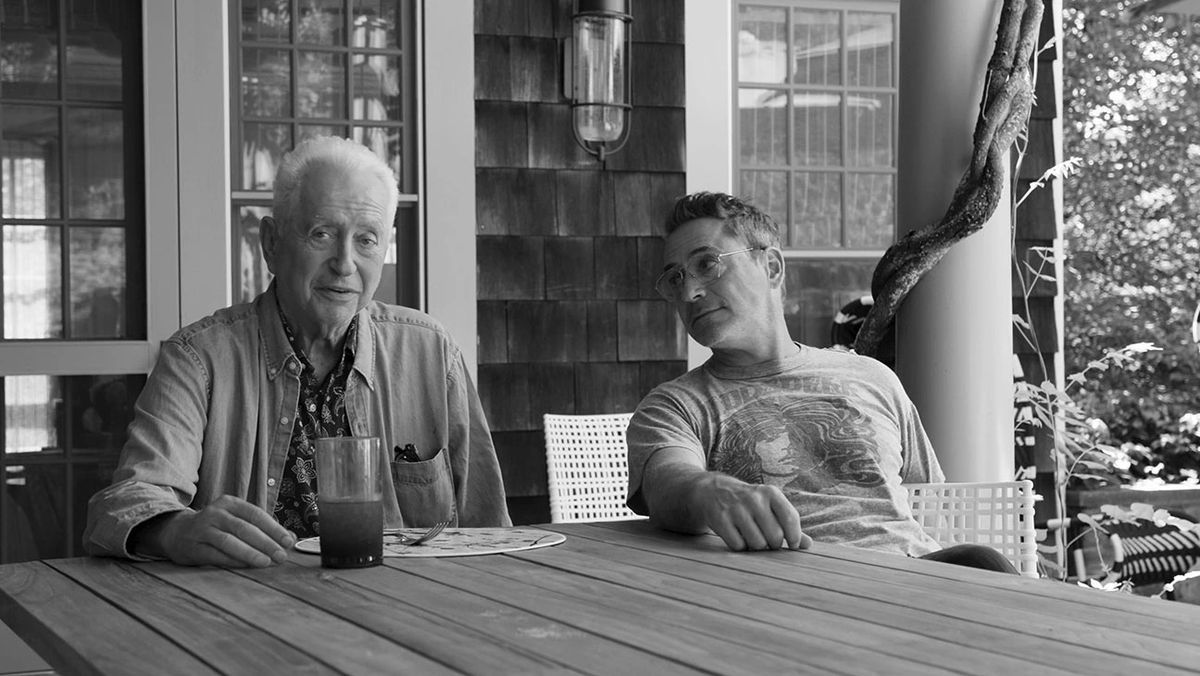 Robert Downey Jr. guarda amorevolmente suo padre mentre si siedono a un tavolo in un'immagine in bianco e nero.
