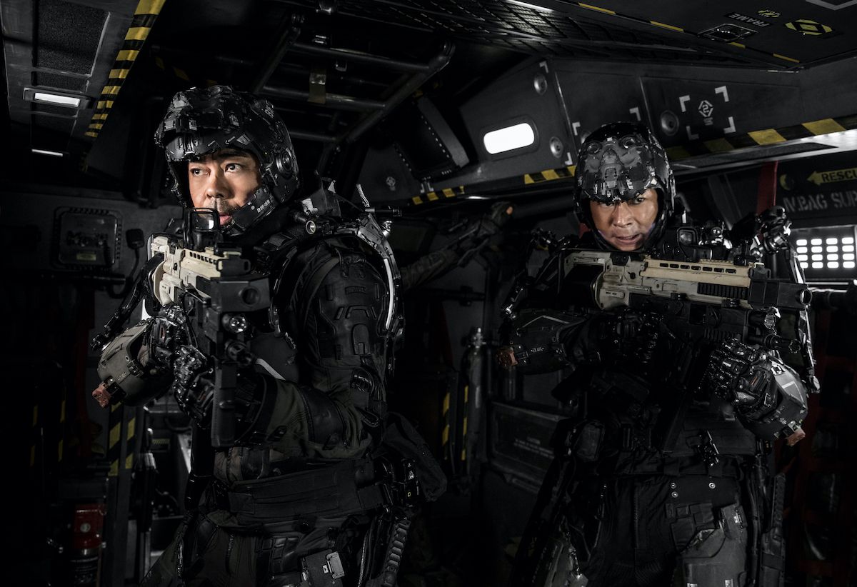 Due uomini in tuta nera armati di fucili in un corridoio industriale fantascientifico.