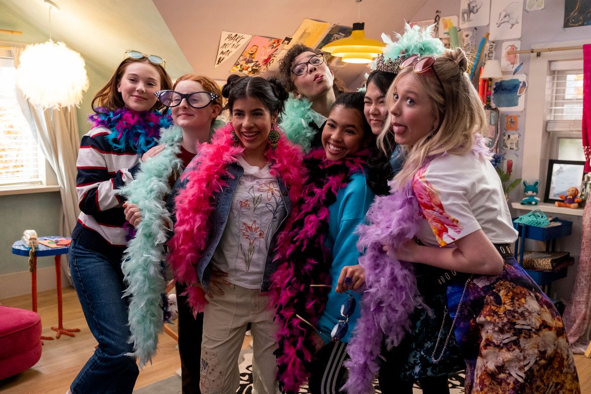 Un gruppo di ragazze adolescenti che indossano boa di piume colorate e occhiali oversize che ridono, tirano fuori la lingua e posano per le foto.