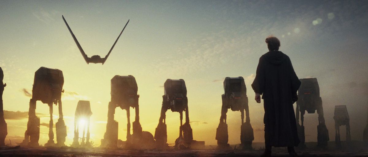 Un aereo si libra dietro un gruppo di AT-AT su un pianeta illuminato dal sole, mentre Luke Skywalker si trova di fronte a loro in The Last Jedi.