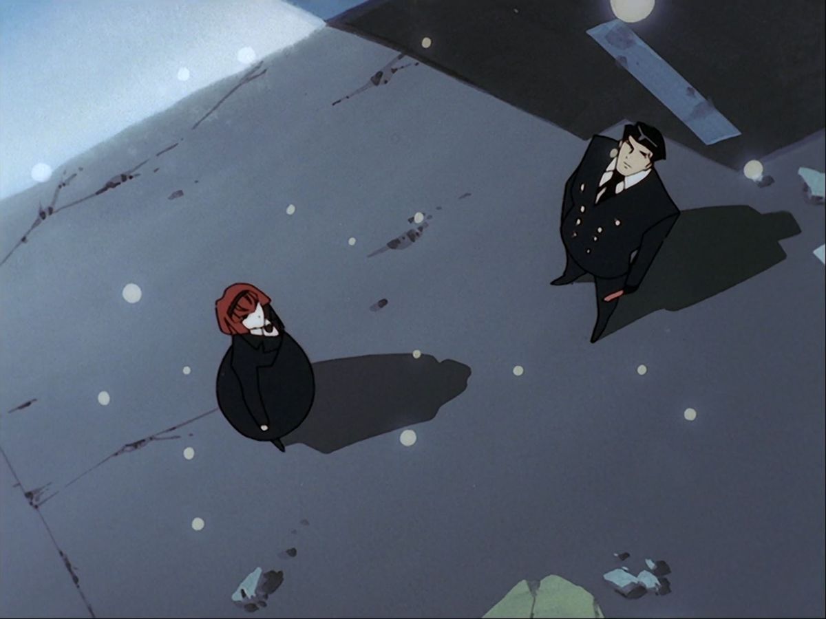 Un uomo in abito nero e una giovane donna in abito nero alzano lo sguardo mentre la neve cade dal cielo.