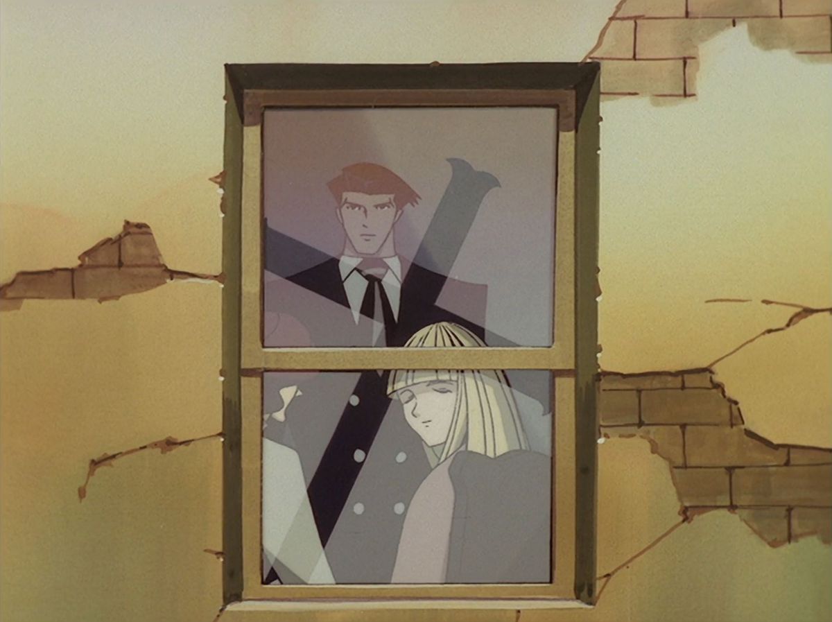Un uomo in abito nero e una giovane donna dai corti capelli biondi fissano il campanile storto di una chiesa incorniciato contro il vetro di una finestra.