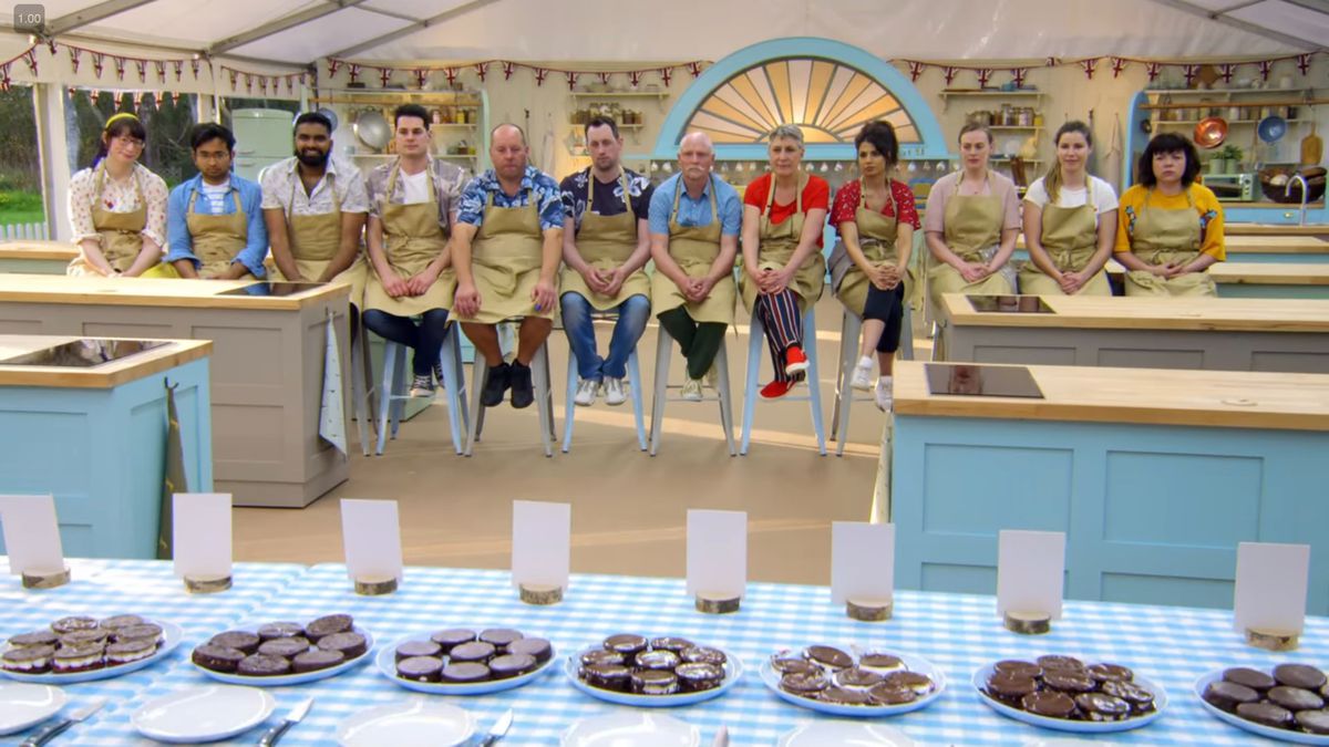 Il cast della stagione 9 di Great British Bake Off seduto in fila durante la valutazione di una sfida tecnica in cui è stato chiesto loro di cuocere le ruote del carro.