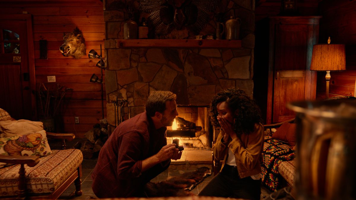 Un ragazzo bianco con la barba (Justin Miles) propone a una donna di colore con i capelli più lunghi (Andrea Laing) davanti a un fuoco scoppiettante in una capanna di tronchi 
