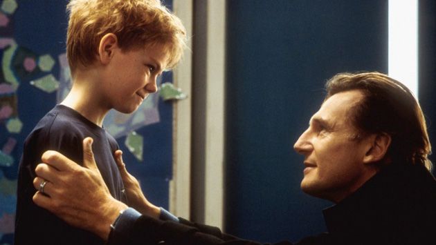 Liam Neeson si inginocchia davanti a un ragazzino, esortandolo a confessare la sua cotta
