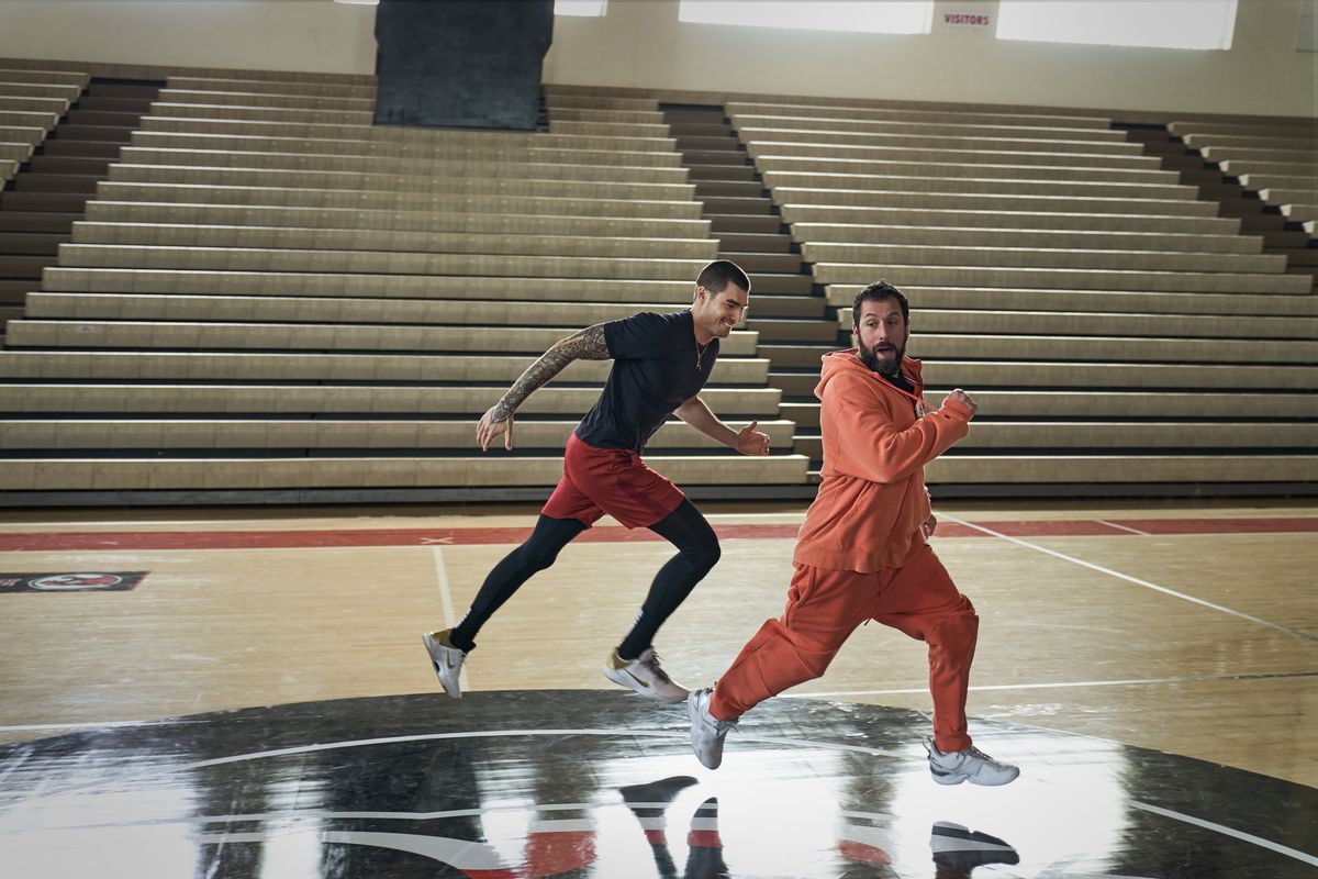 Adam Sandler, con indosso una tuta arancione, corre su un campo da basket accanto a un sorridente Juancho Hernangómez in Hustle.