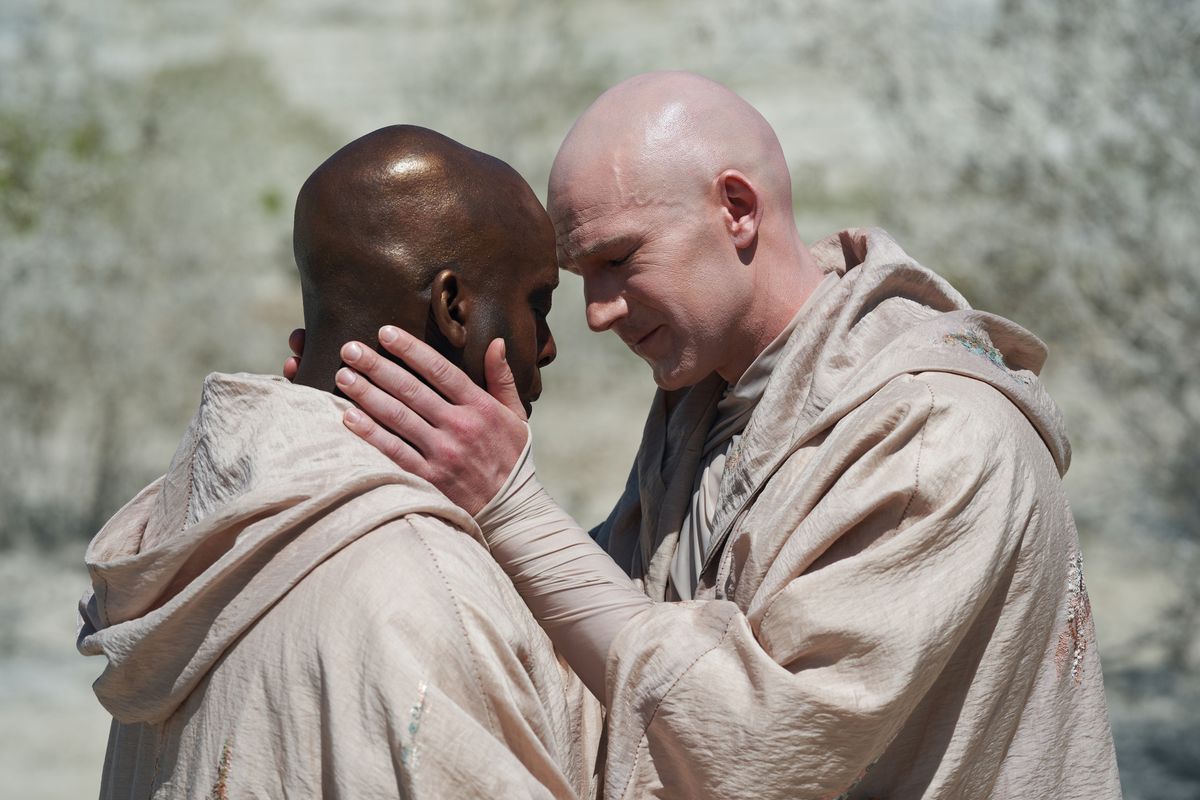 Due uomini (Kobna Holdbrook-Smith, Simon Harrison) si toccano la fronte in un fotogramma della stagione 3 di His Dark Materials