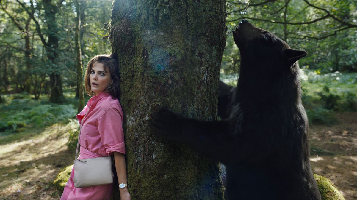 Sari (Keri Russell), una donna dall'aria terrorizzata con un vestito rosa, si nasconde dietro un albero mentre un orso ubriaco di cocaina annusa dall'altra parte in Cocaine Bear