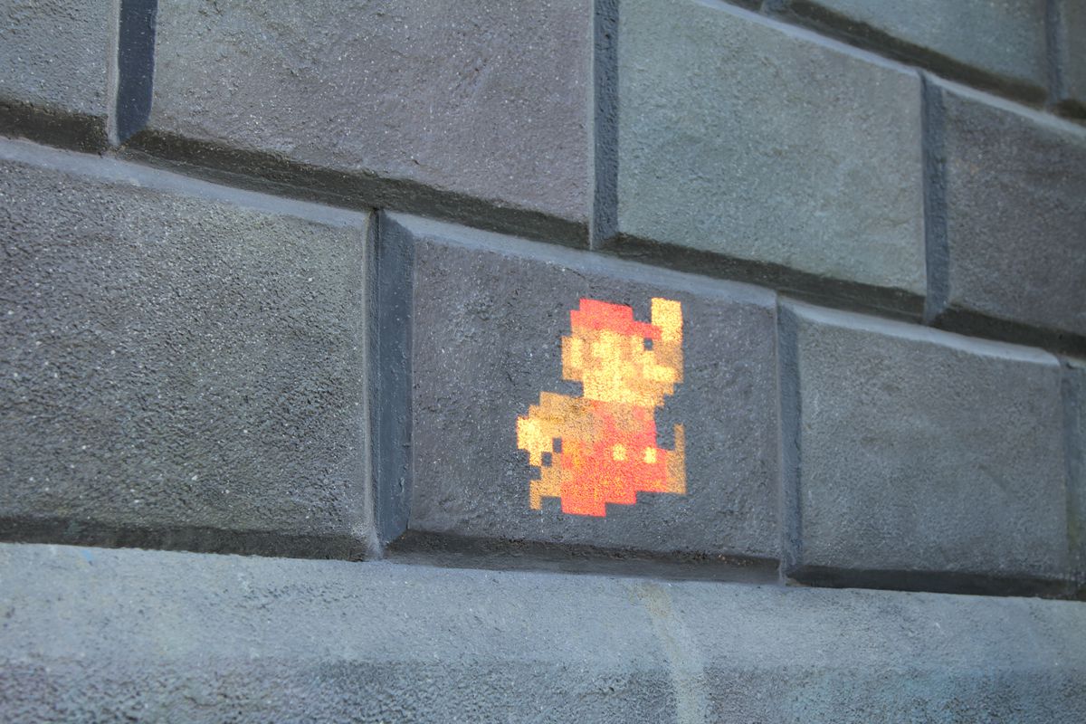 Una proiezione di Mario pixelato sullo sfondo di un muro di mattoni.