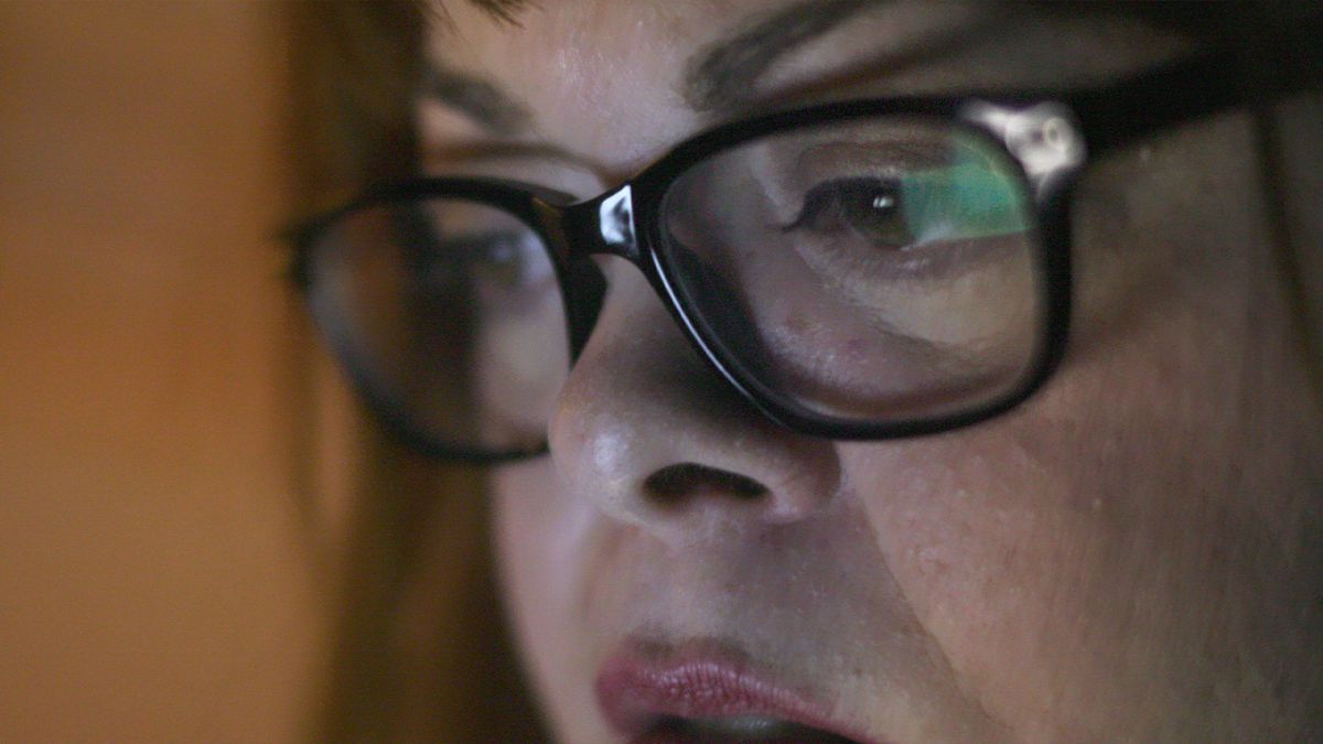 Un'immagine ravvicinata di una donna che indossa gli occhiali mentre fissa uno schermo.