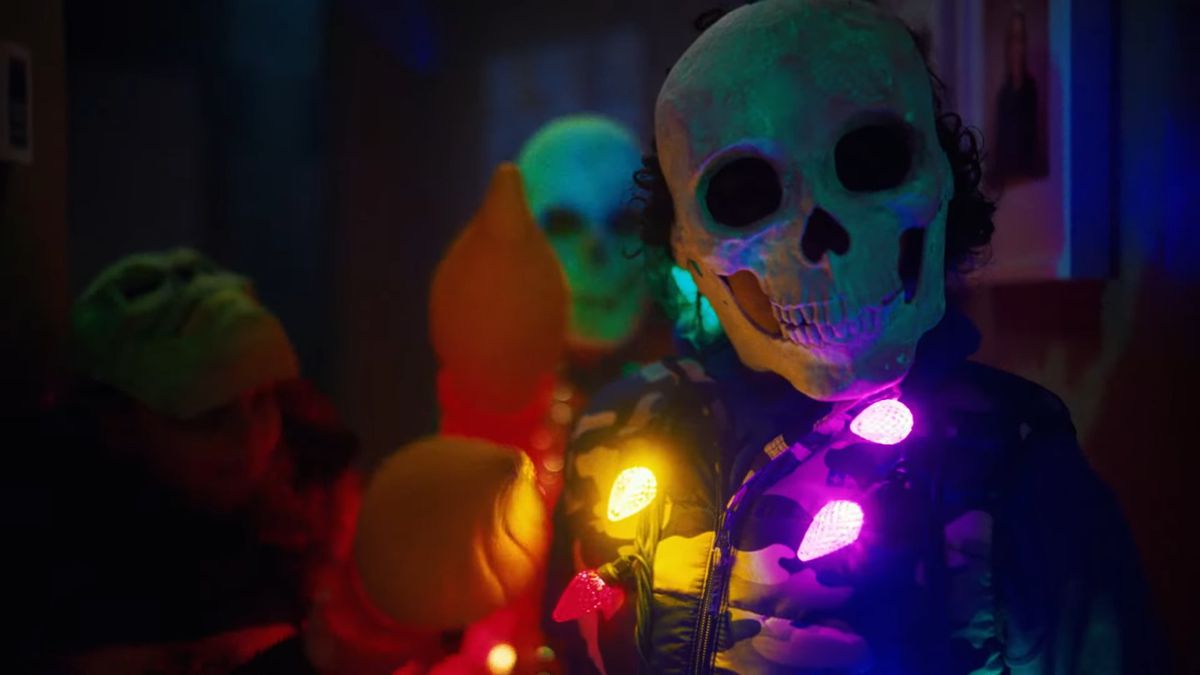 Una persona che indossa una maschera con la faccia da teschio e un costume elaborato con luci multicolori sparse intorno al collo.