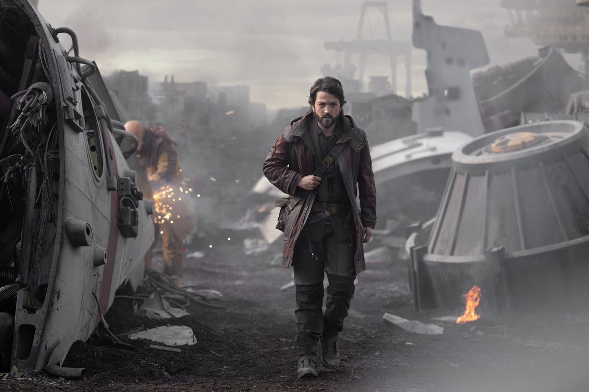Diego Luna nei panni di Cassian Andor attraversa un campo di rottami, con macchine rotte e in fiamme.