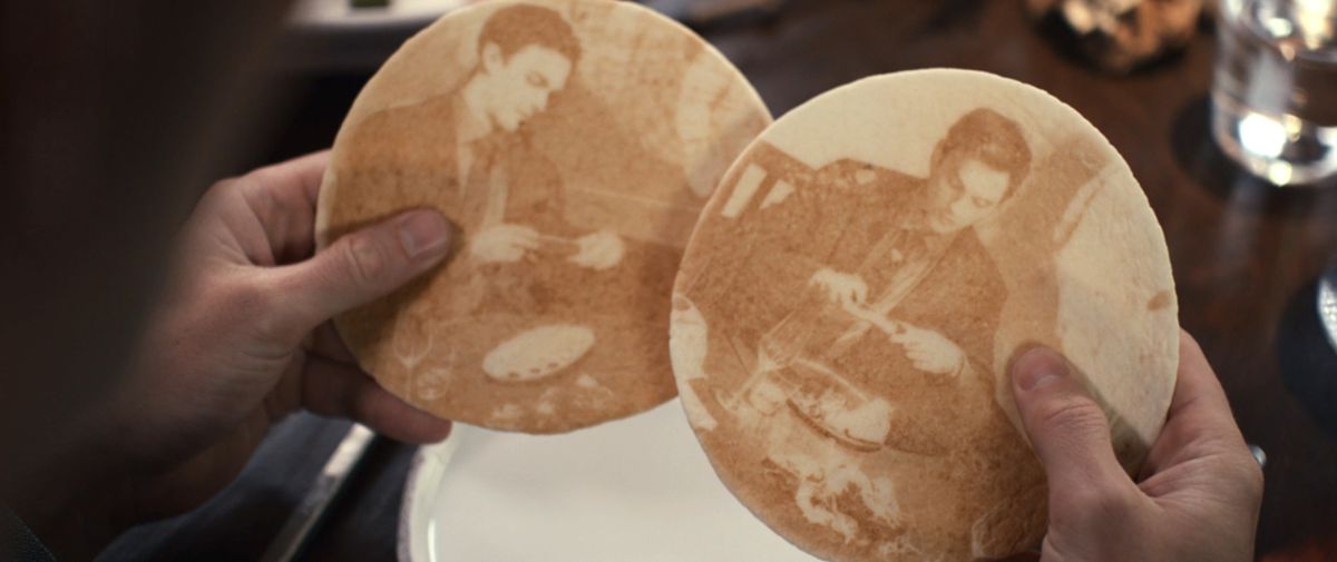 Due pezzi di focaccia con immagini di Nicholas Hoult che scatta foto del suo cibo con l'iPhone in The Menu