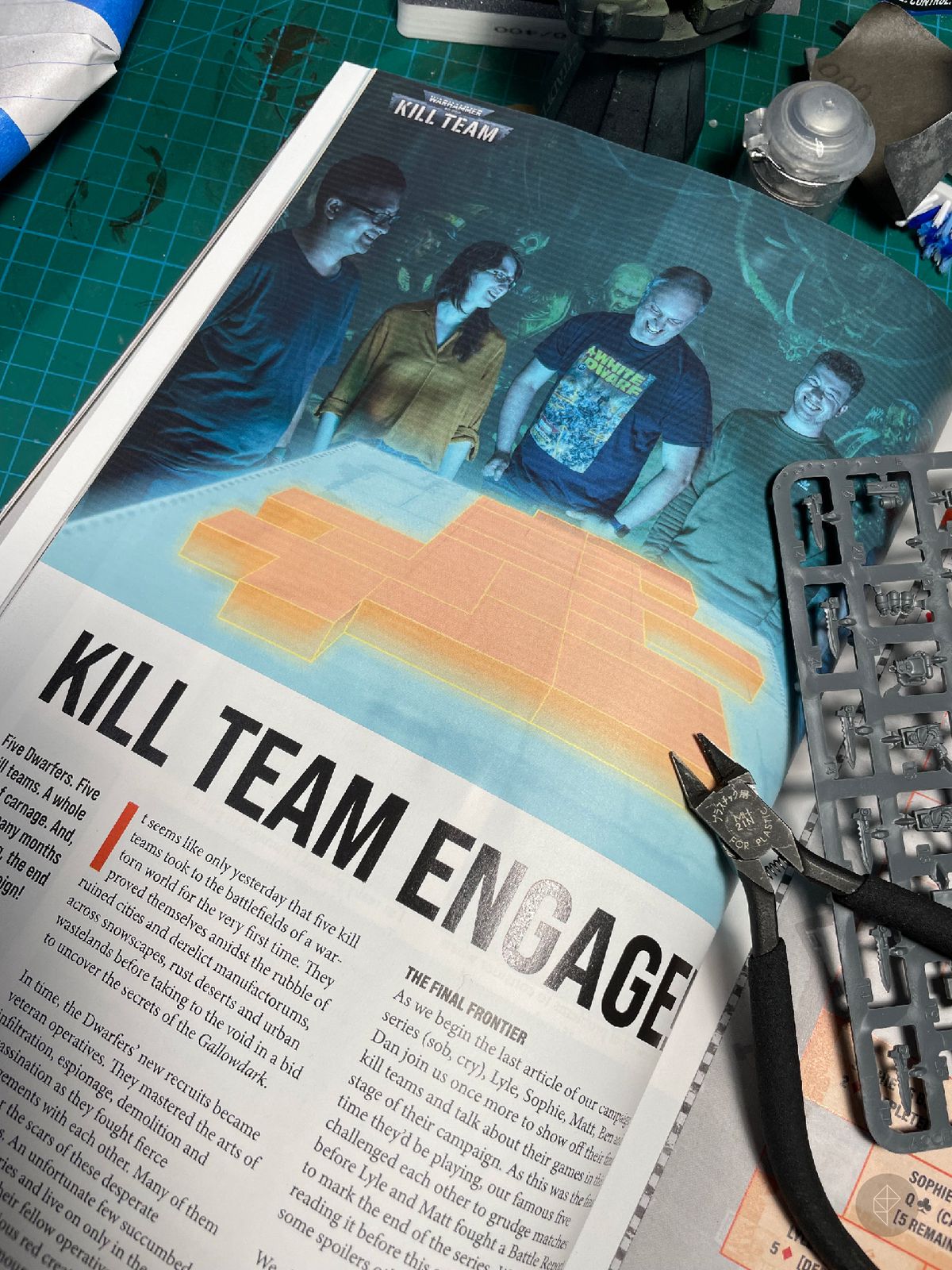 Una pagina di White Dwarf che mostra un gruppo di giocatori attorno a una mappa virtuale di Kill Team.