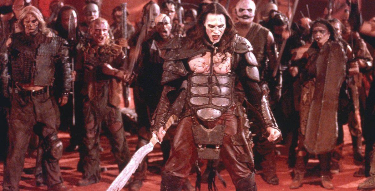 Un guerriero dai capelli lunghi con la pelle pallida vestito con un'armatura e con in mano una spada si trova di fronte a un'orda di soldati simili a zombi.