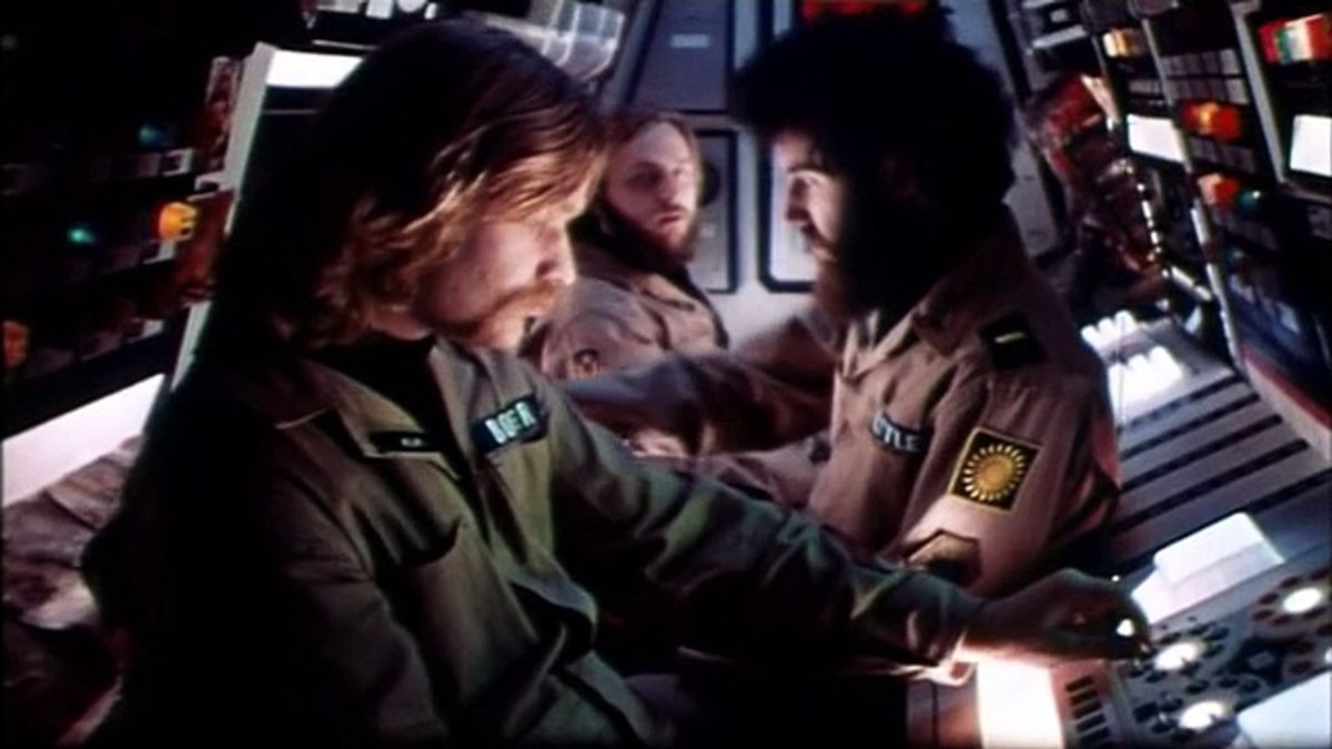 Tre uomini in uniformi uguali siedono schiena contro schiena l'uno contro l'altro nell'angusta cabina di pilotaggio di un'astronave.