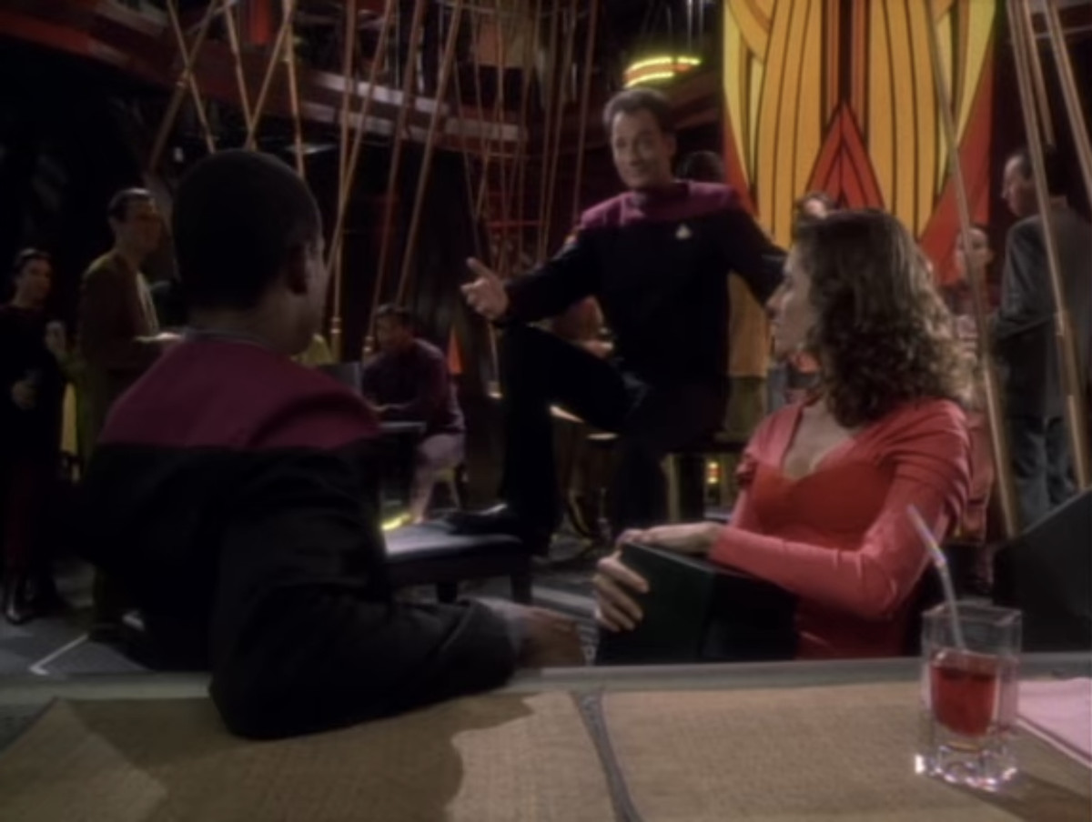 Q tiene le braccia aperte al bar al Capitano in Star Trek: Deep Space Nine