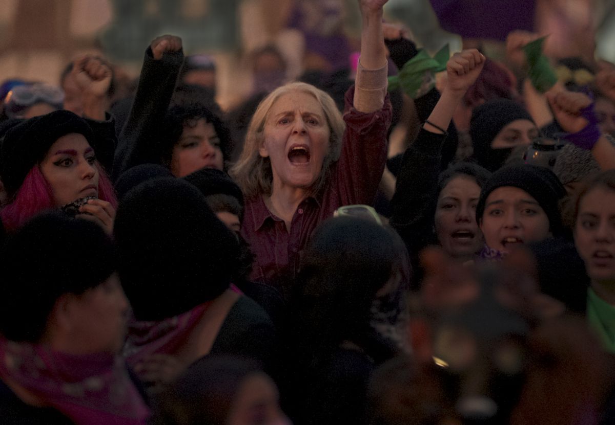 Una donna anziana con i capelli grigi che urla e alza il pugno in mezzo a una folla di donne arrabbiate.