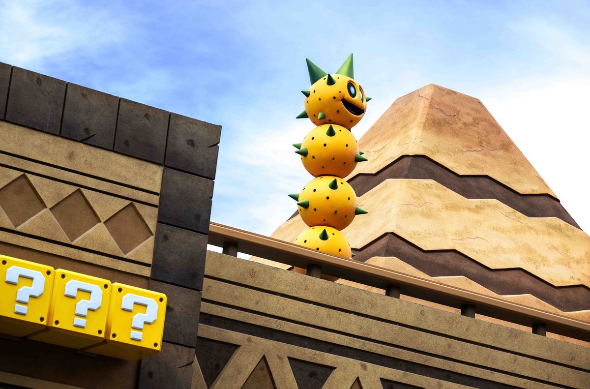 Una foto dal Super Nintendo World, con un alto Pokey davanti a una piramide e blocchi di monete in primo piano.