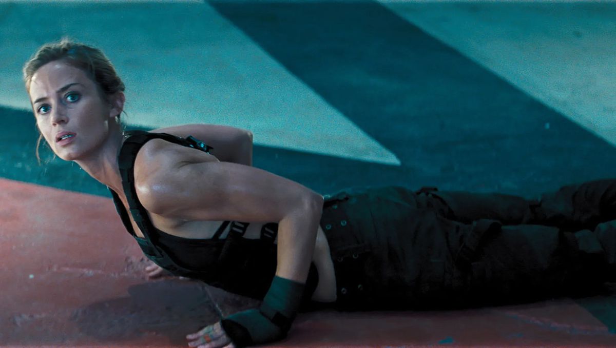 Una donna (Emily Blunt) si solleva dal pavimento di un'area di allenamento dopo aver fatto una serie di flessioni.
