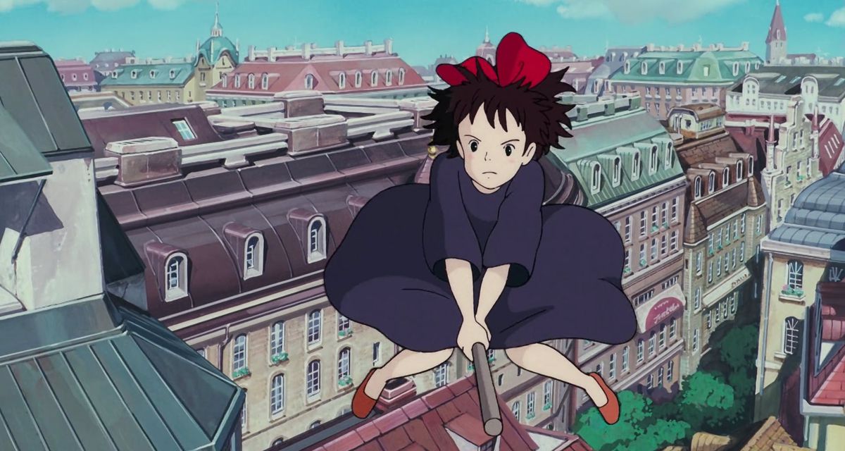 Kiki, una ragazza anime con i capelli neri e un fiocco rosso in cima, cavalca una scopa su un paesaggio urbano in stile europeo in Kiki's Delivery Service dello Studio Ghibli.