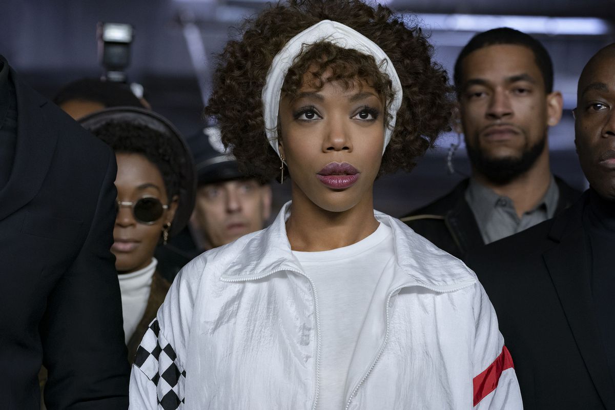 Naomi Ackie veste tutta di bianco, con una fascia bianca, ed è circondata da guardie di sicurezza nei panni di Whitney Houston in I Wanna Dance With Somebody.