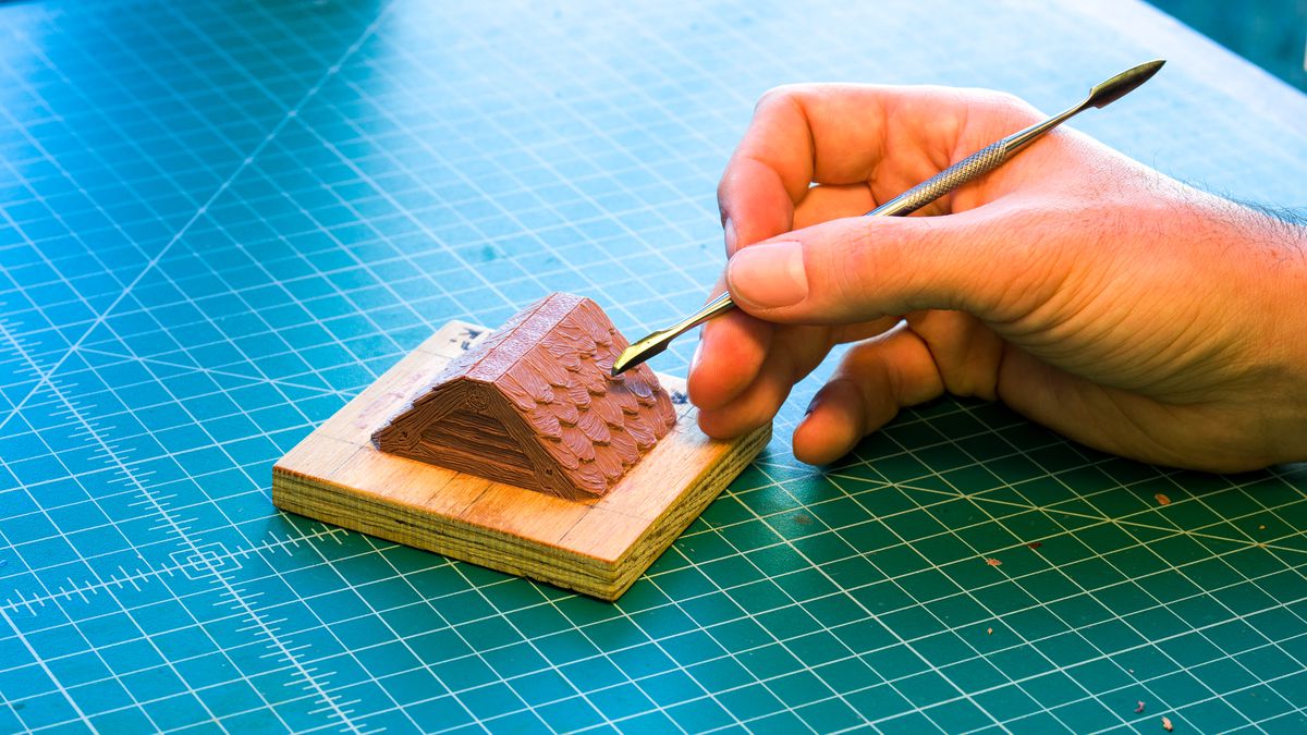 Una mano che si protende con uno strumento di metallo per creare la versione originale di una sezione del tetto di Dwarven Forge.