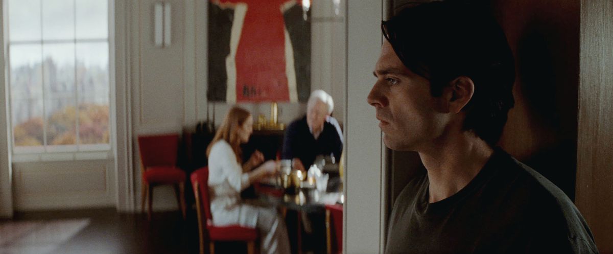 Un profilo laterale di Sebastian Stan che sembra abbandonato, mentre Julianne Moore e John Lithgow cenano sfocati a un tavolo sullo sfondo.