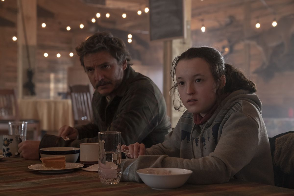 Pedro Pascal e Bella Ramsey siedono insieme a un tavolo con del cibo in The Last of Us.