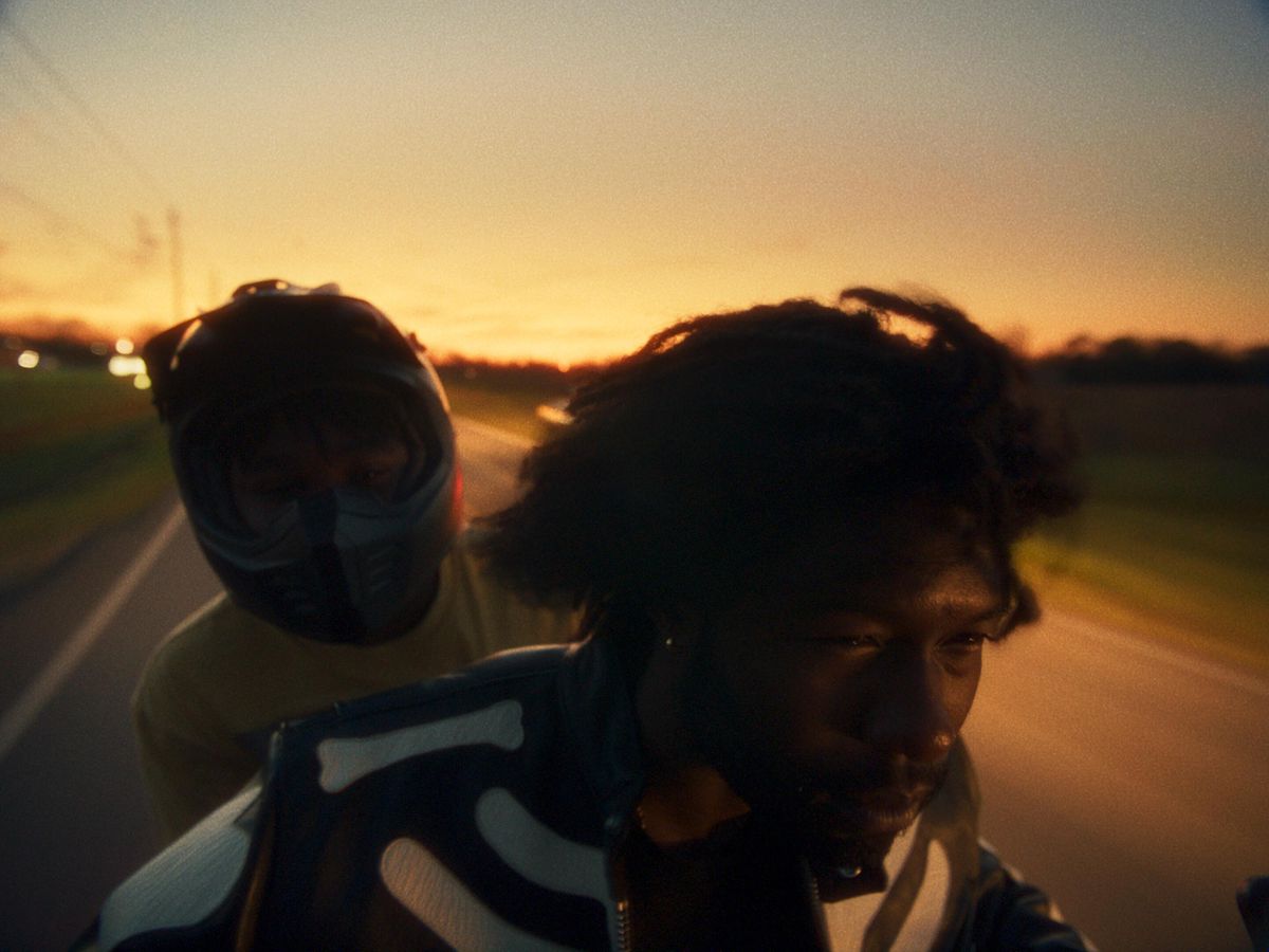 Un adolescente (Jalyn Hall) che indossa un casco cavalca sul retro di una motocicletta guidata da un uomo con lunghi dreadlock fluenti (Trevante Rhodes).