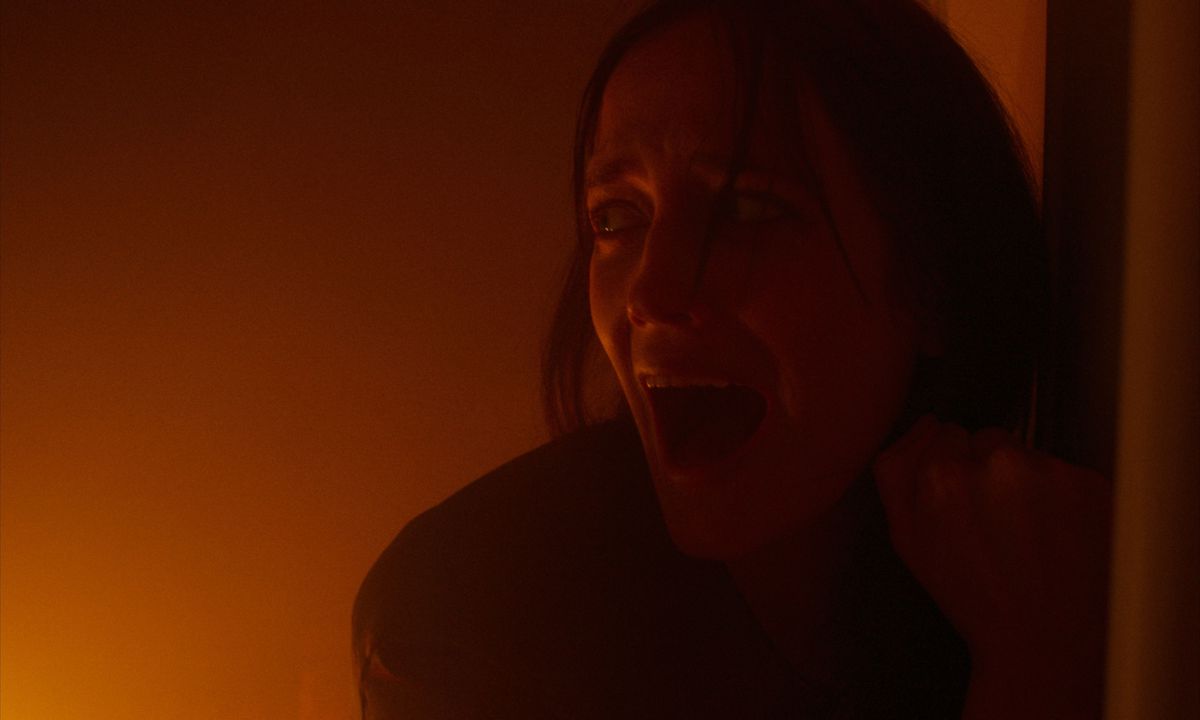 Una donna urlante (Eva Green) si appoggia a un muro lontano da un bagliore rosso simile a un fuoco fuori dallo schermo.