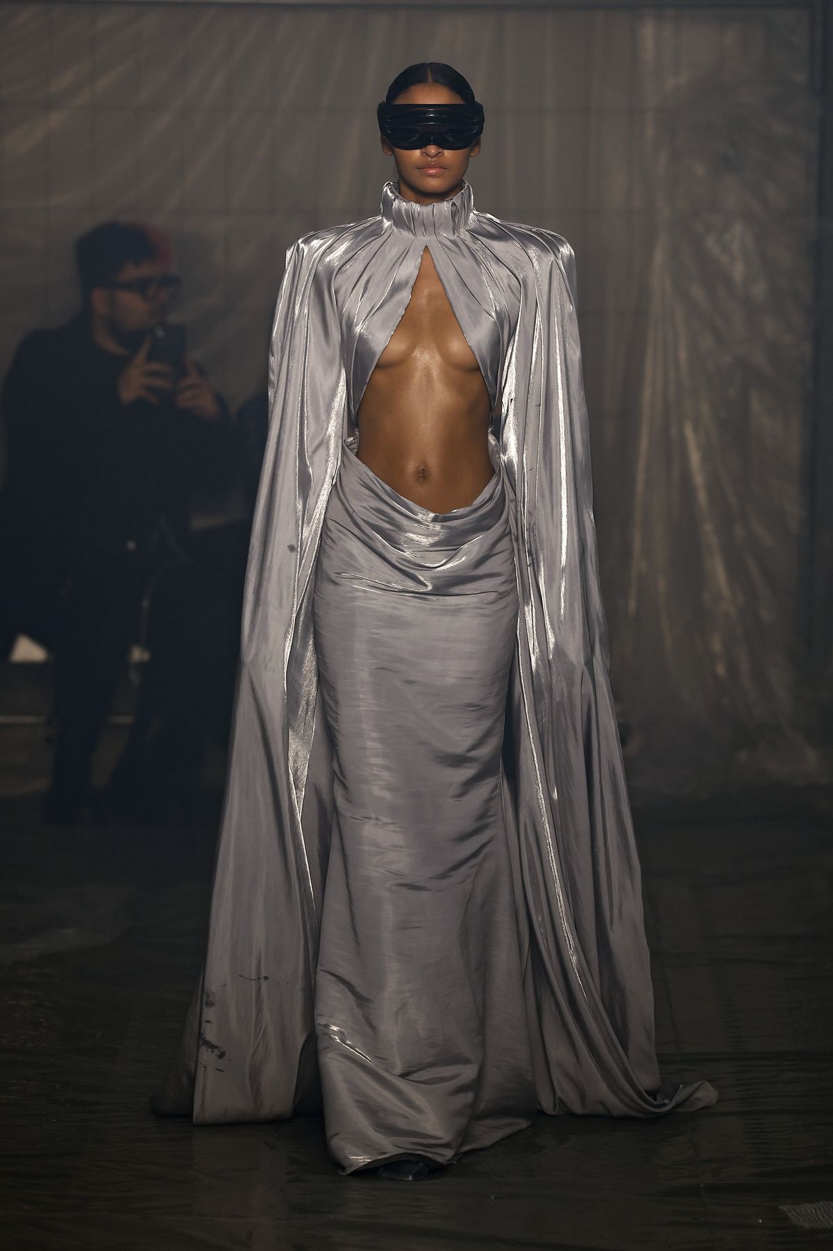 Una modella che indossa un abito grigio fluente con l'ombelico esposto cammina sulla passerella della sfilata di Han Kjobenhavn alla settimana della moda di Milano.