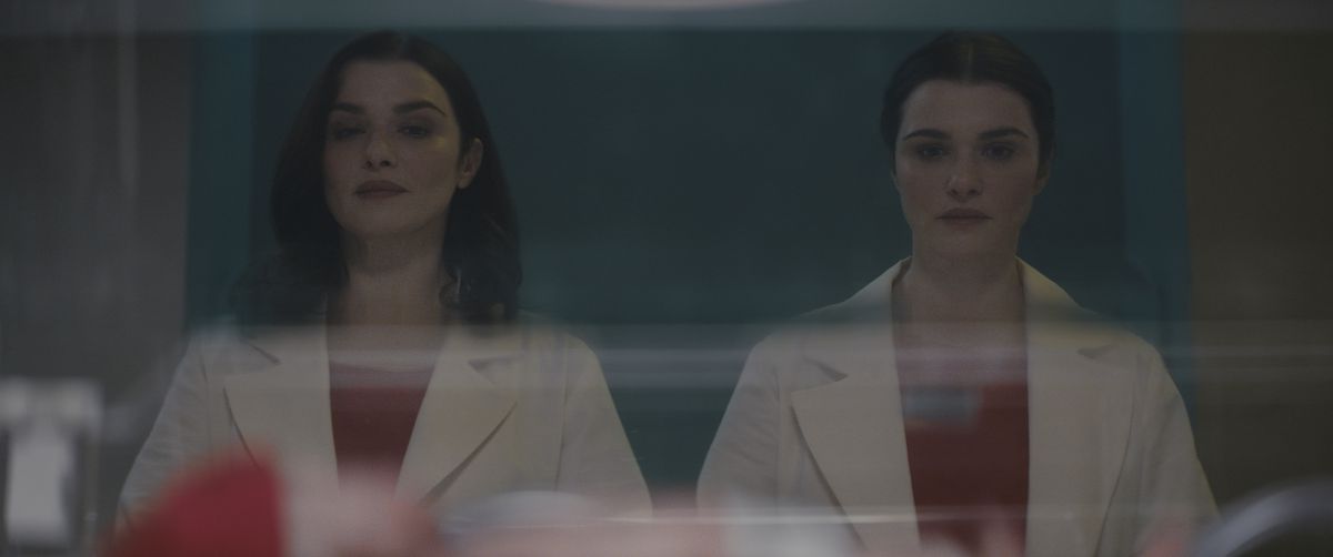 Due donne identiche (Rachel Weisz) stanno una accanto all'altra in abiti da dottore bianchi abbinati che fissano un bambino in una culla dell'ospedale.