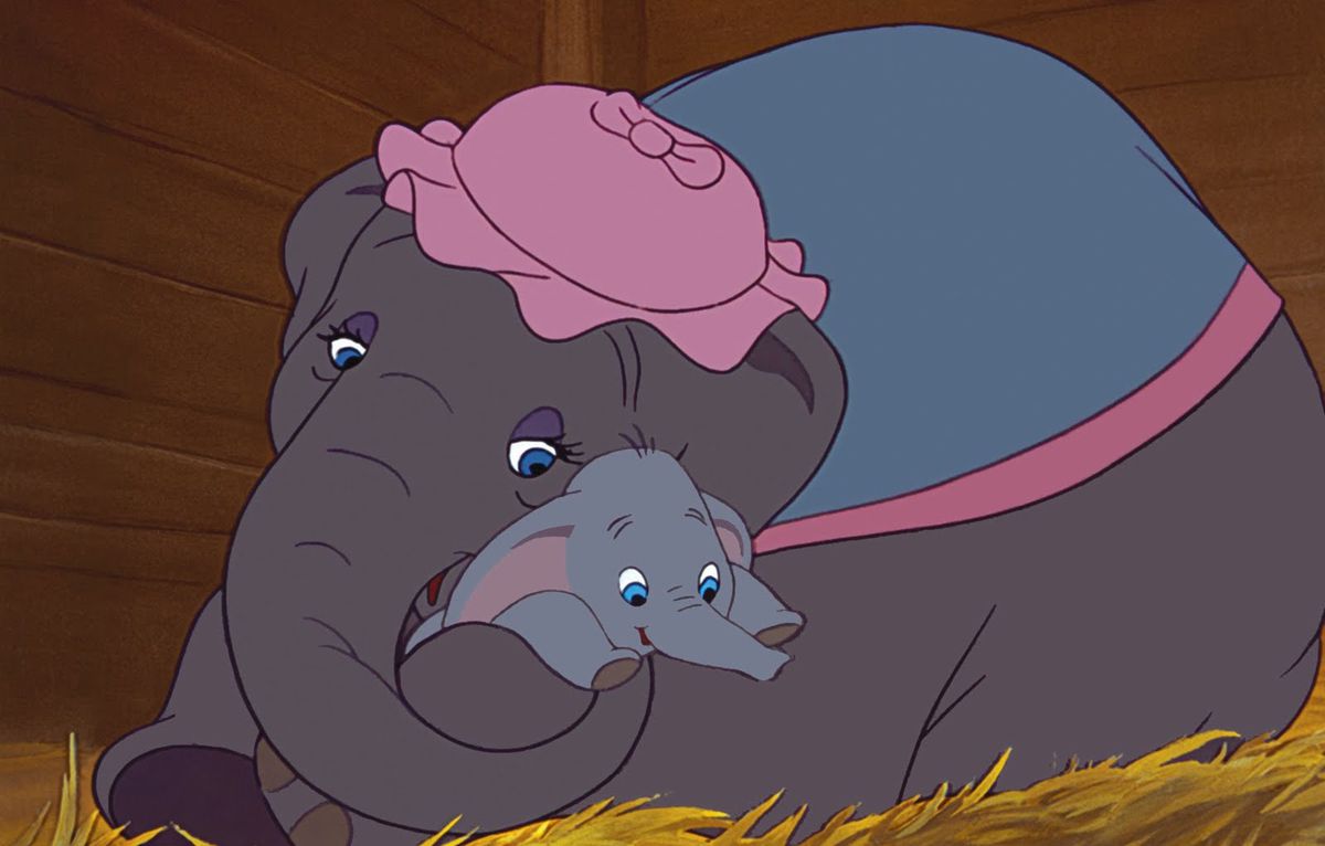 La signora Jumbo, un elefante con un berretto rosa e uno scialle blu, culla il suo piccolo Dumbo nella sua proboscide mentre giace su un letto di paglia nel film d'animazione del 1941 Dumbo