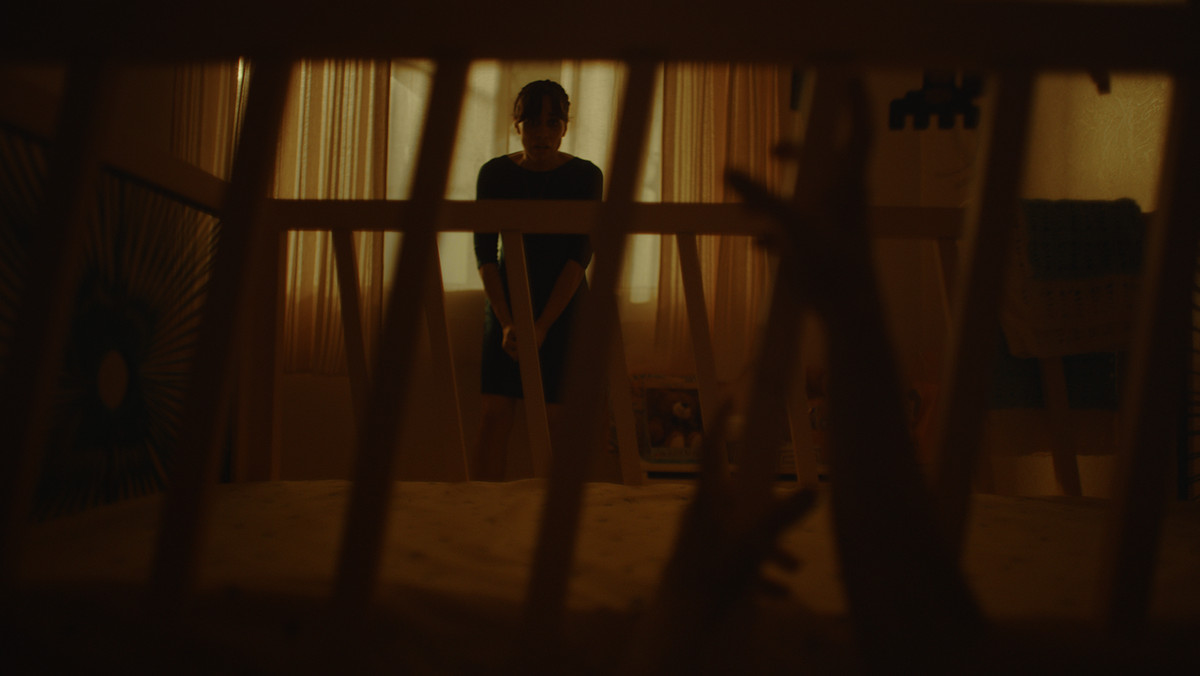 Valeria si rannicchia nell'angolo di un asilo nido mentre mani artigliate si allungano attraverso una culla nel film horror Huesera: The Bone Woman