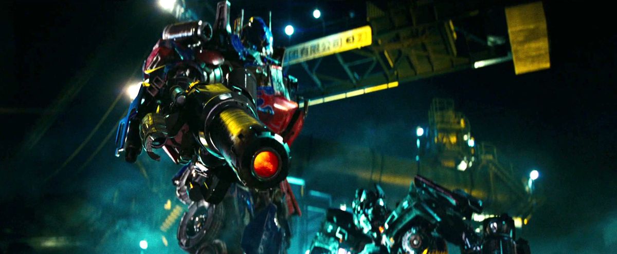 Optimus Prime solleva una pistola e preme il grilletto mentre un altro Transformer guarda in Revenge of the Fallen