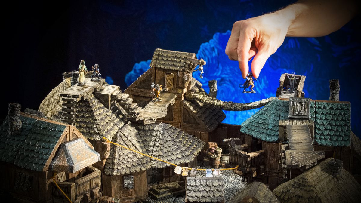 Una mano raggiunge un diorama sul tetto per strappare una miniatura dalla passerella di un edificio.