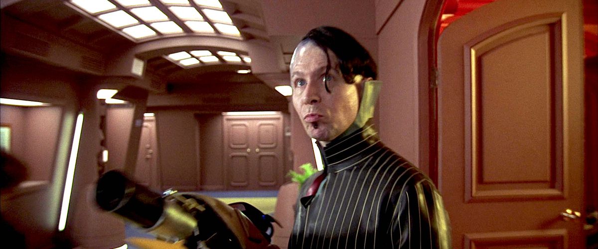 Zorg brandisce un'arma aliena mentre si precipita nel corridoio di un corridoio di un hotel