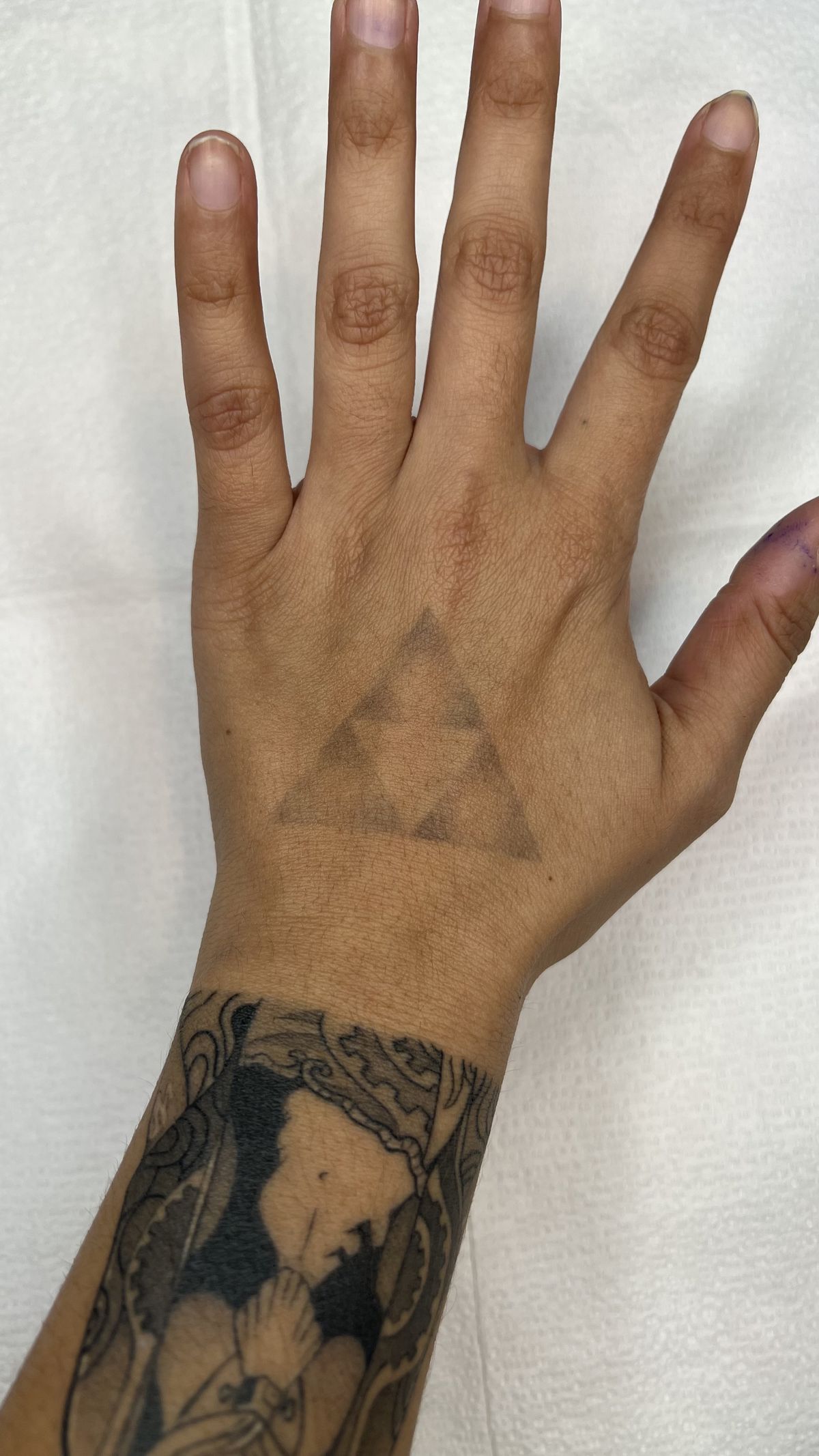 Un debole tatuaggio della Triforza sulla mano di una persona