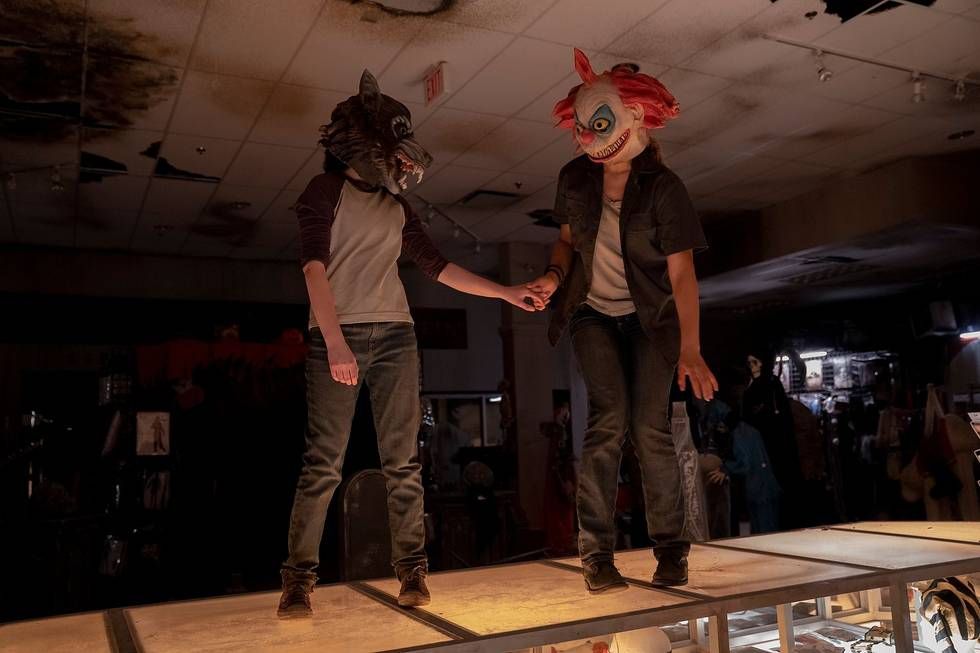 Ellie (Bella Ramsey) e Riley (Storm Reid) in piedi sul bancone di un negozio di Halloween e si tengono per mano incerte mentre indossano rispettivamente una maschera da lupo mannaro e una da clown