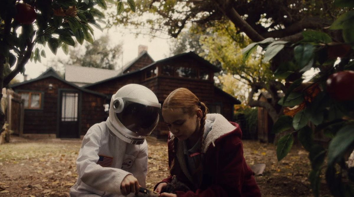 Una giovane ragazza siede accanto a un ragazzo che indossa una tuta da astronauta fuori di fronte a una casa in Spoonful of Sugar.